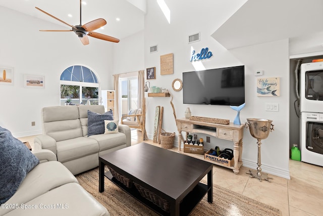 living area featuring a towering ceiling, light tile patterned floors, visible vents, and stacked washer / drying machine