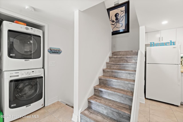 laundry area featuring stacked washer and clothes dryer, light tile patterned floors, baseboards, and laundry area