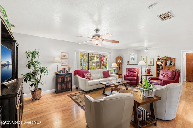 living room with light wood finished floors, baseboards, visible vents, a ceiling fan, and a textured ceiling