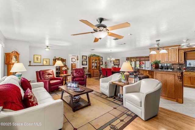 living room with ceiling fan with notable chandelier and light wood-style flooring