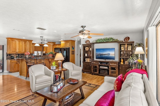 living room with visible vents, ceiling fan, light wood-style flooring, and a textured ceiling