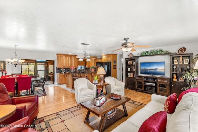 living area with light wood-type flooring, visible vents, and ceiling fan with notable chandelier