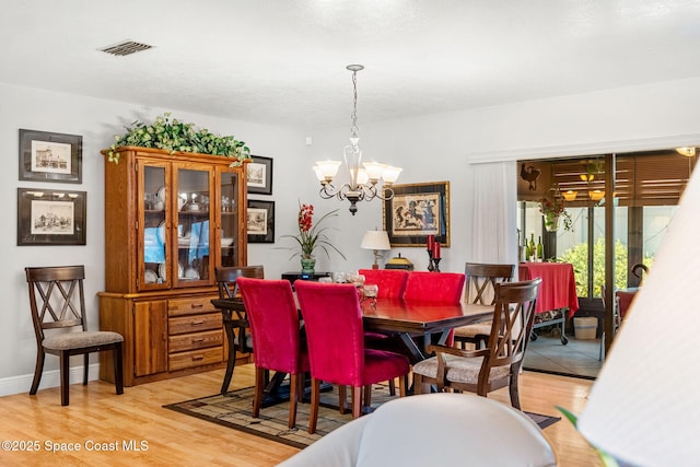 dining space with baseboards, visible vents, a notable chandelier, and light wood finished floors