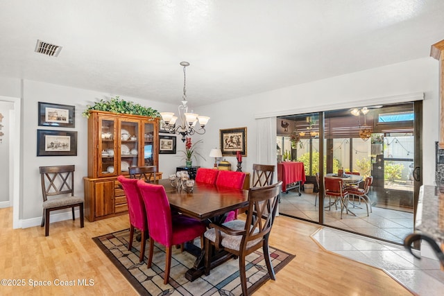 dining area featuring light wood-type flooring, baseboards, visible vents, and a notable chandelier