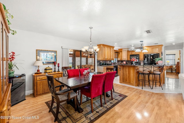 dining room featuring baseboards, light wood finished floors, visible vents, and an inviting chandelier