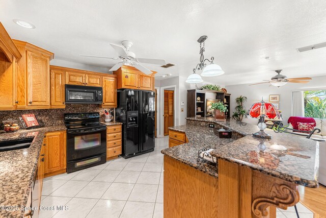 kitchen with light tile patterned floors, a ceiling fan, dark stone countertops, black appliances, and backsplash