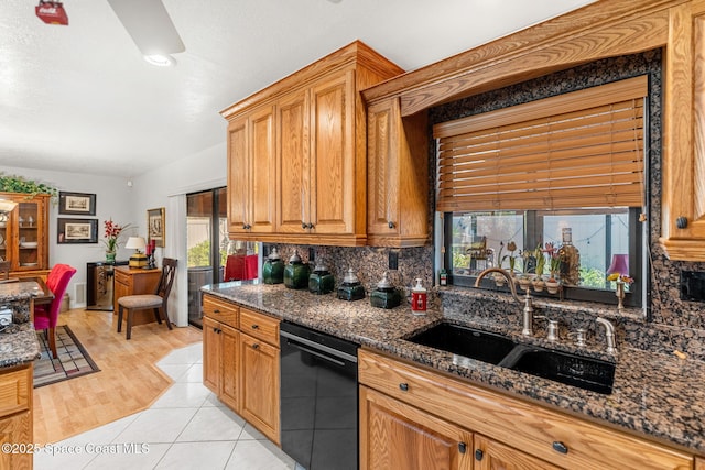 kitchen featuring black dishwasher, tasteful backsplash, dark stone countertops, and a sink