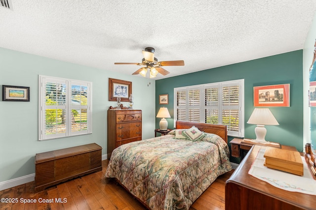 bedroom with a textured ceiling, visible vents, a ceiling fan, baseboards, and hardwood / wood-style floors