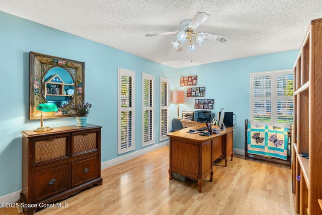 office space with baseboards, a textured ceiling, a ceiling fan, and light wood-style floors