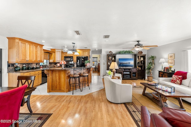 living area with light wood finished floors, visible vents, and a ceiling fan