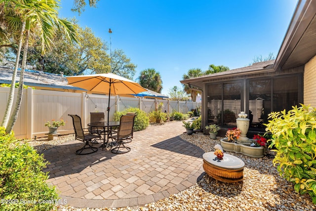 view of patio with a sunroom, a fenced backyard, and outdoor dining area