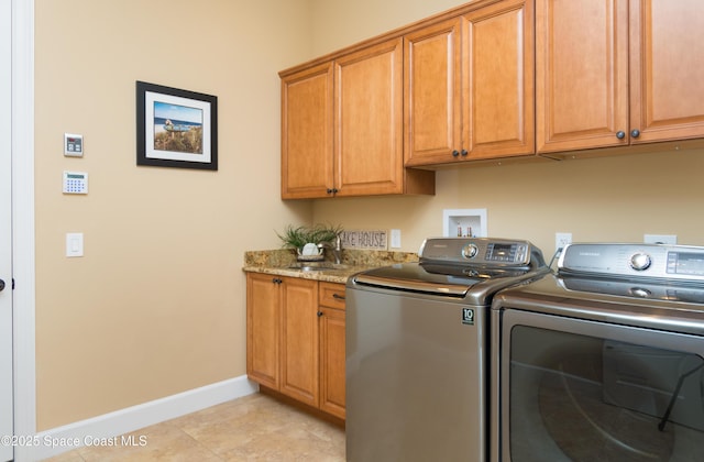 washroom featuring cabinet space, light tile patterned floors, baseboards, washer and dryer, and a sink