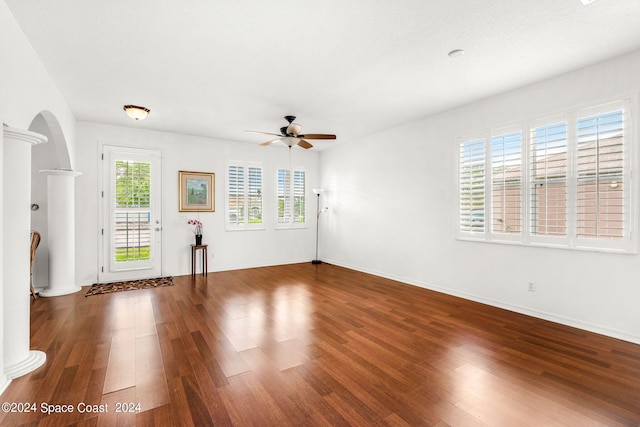 unfurnished living room with arched walkways, ornate columns, ceiling fan, wood finished floors, and baseboards