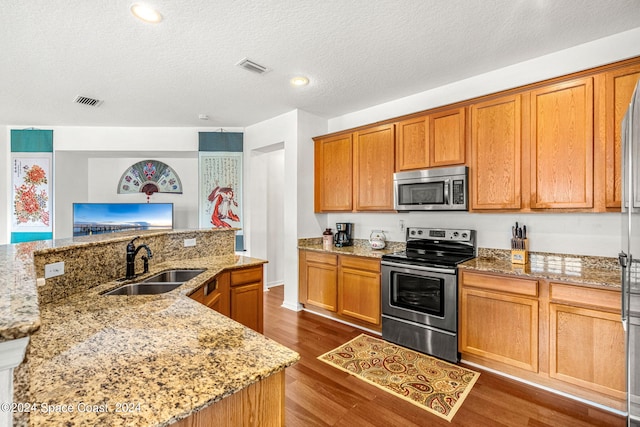 kitchen with appliances with stainless steel finishes, dark wood finished floors, a sink, and light stone countertops