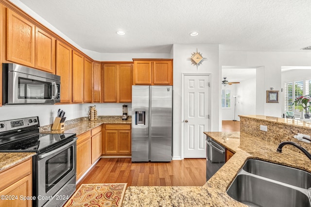 kitchen with light stone countertops, a sink, light wood-style floors, appliances with stainless steel finishes, and brown cabinets