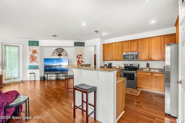 kitchen featuring dark wood-style floors, brown cabinets, a breakfast bar area, stainless steel appliances, and visible vents