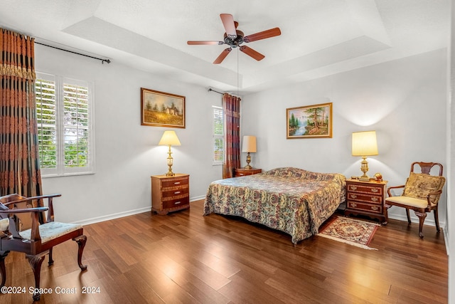 bedroom featuring a tray ceiling, baseboards, and wood finished floors