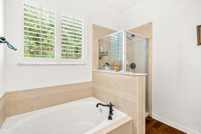 bathroom with a stall shower, baseboards, a bath, and wood finished floors