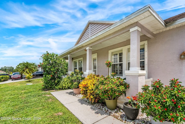 view of exterior entry featuring covered porch, a yard, and stucco siding