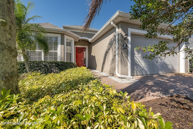 doorway to property featuring an attached garage, driveway, and stucco siding