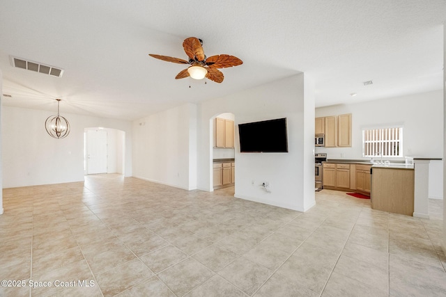 unfurnished living room with arched walkways, ceiling fan with notable chandelier, and visible vents