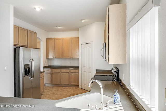 kitchen featuring light tile patterned floors, arched walkways, stainless steel appliances, light brown cabinetry, and a sink