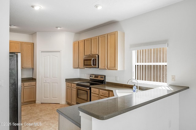 kitchen with appliances with stainless steel finishes, dark countertops, a sink, and a peninsula