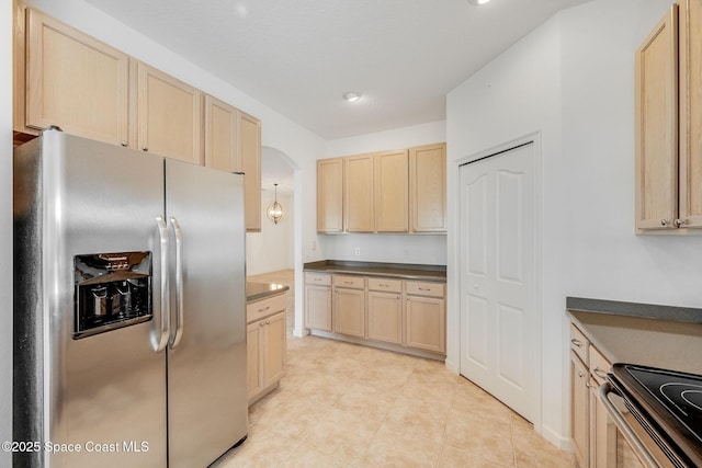 kitchen with stainless steel fridge, range with electric cooktop, arched walkways, dark countertops, and light brown cabinetry