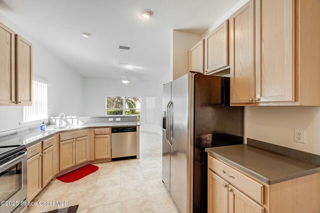 kitchen featuring visible vents, appliances with stainless steel finishes, a peninsula, light brown cabinetry, and a sink