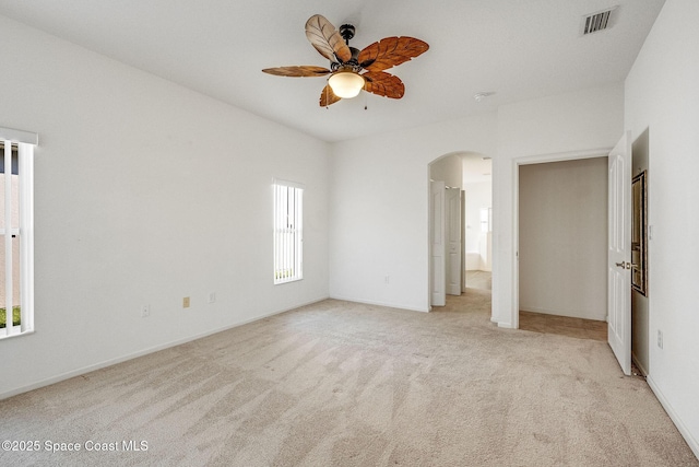 unfurnished bedroom with baseboards, visible vents, arched walkways, a ceiling fan, and light colored carpet