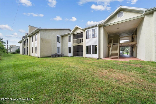 rear view of property with stairs, a lawn, and stucco siding