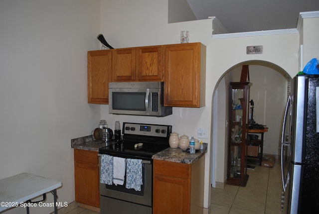 kitchen featuring arched walkways, crown molding, appliances with stainless steel finishes, brown cabinetry, and light tile patterned flooring