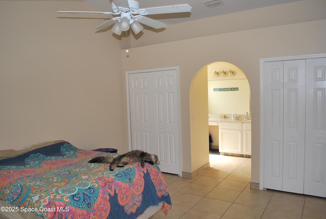 bedroom with light tile patterned floors, visible vents, arched walkways, a ceiling fan, and a sink