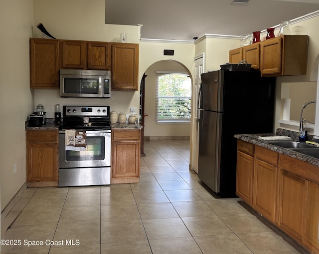 kitchen featuring stainless steel appliances, dark countertops, brown cabinetry, and a sink