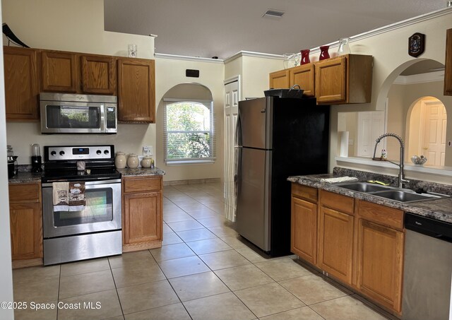 kitchen featuring appliances with stainless steel finishes, a sink, arched walkways, brown cabinetry, and ornamental molding