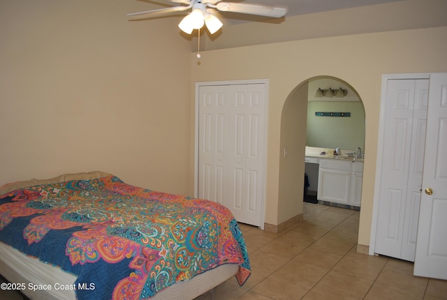 bedroom featuring a ceiling fan, arched walkways, a sink, multiple closets, and light tile patterned flooring