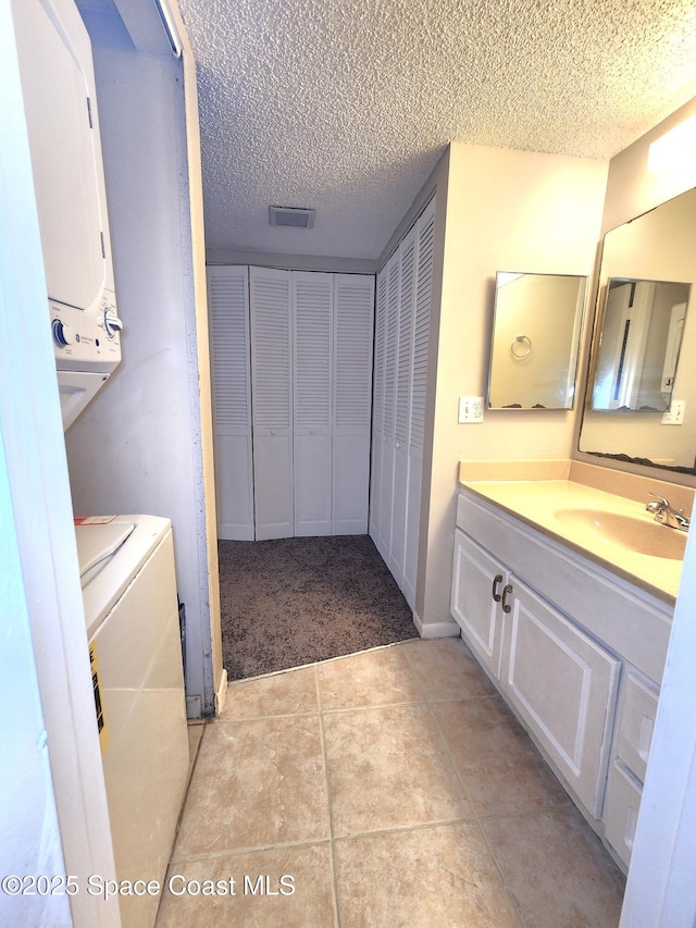 bathroom featuring tile patterned floors, a textured ceiling, vanity, stacked washing maching and dryer, and a closet