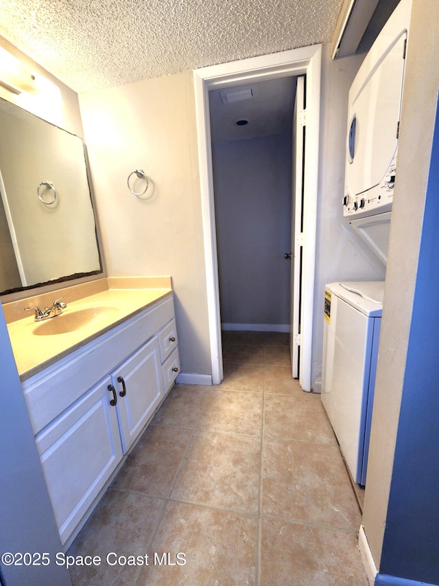 bathroom featuring a textured ceiling, vanity, baseboards, stacked washing maching and dryer, and tile patterned floors