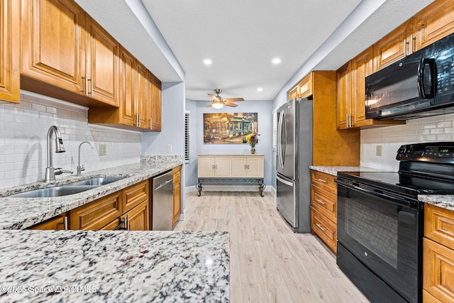 kitchen featuring black appliances, light stone counters, brown cabinetry, and a sink