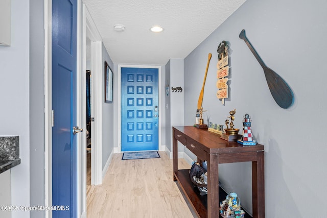 foyer entrance featuring a textured ceiling, light wood-type flooring, and baseboards