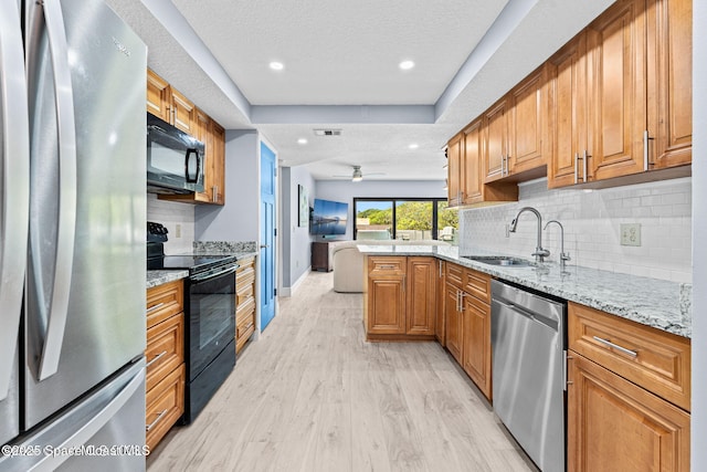 kitchen featuring a peninsula, a sink, light stone countertops, black appliances, and brown cabinetry