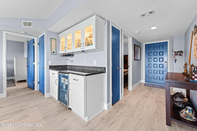 kitchen with glass insert cabinets, white cabinets, visible vents, and light wood finished floors