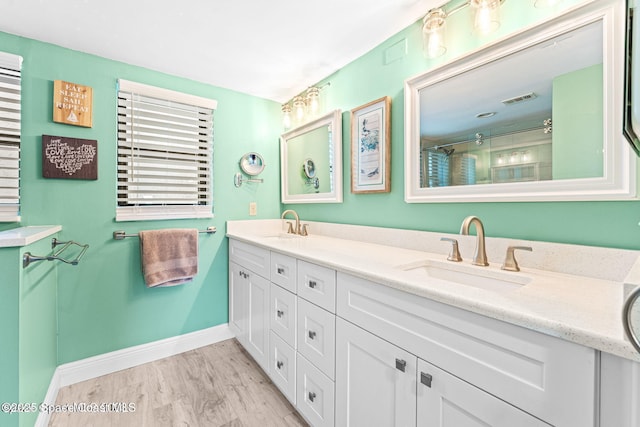 full bath with wood finished floors, a sink, visible vents, baseboards, and double vanity