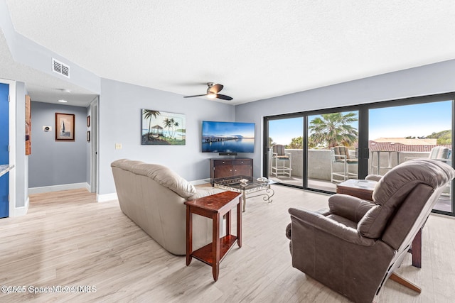 living area featuring a textured ceiling, ceiling fan, visible vents, baseboards, and light wood-style floors