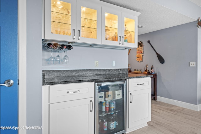 bar featuring a textured ceiling, wine cooler, baseboards, light wood-type flooring, and a bar