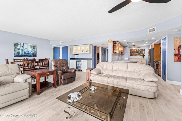 living area featuring beverage cooler, a dry bar, visible vents, and light wood-style floors