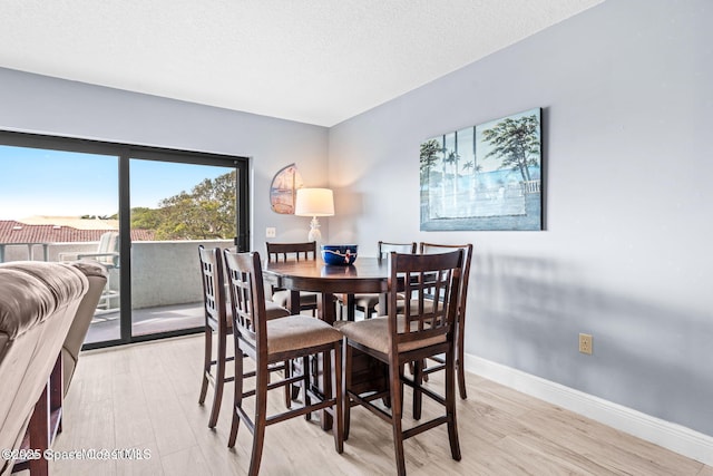 dining space with light wood-style floors, a textured ceiling, and baseboards