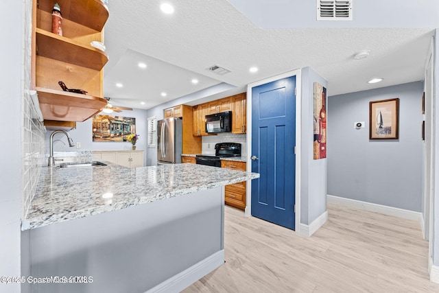 kitchen featuring light stone counters, a peninsula, black appliances, open shelves, and a sink