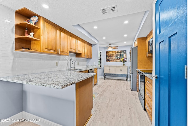 kitchen with light wood-type flooring, black appliances, light stone counters, and a sink