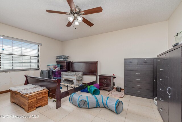 bedroom with ceiling fan, baseboards, a textured ceiling, and light tile patterned flooring